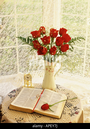 Dutzend rote Rosen im Krug Jubiläums Uhr und aufgeschlagene Bibel Stockfoto