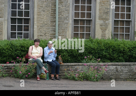 Zwei Frauen sitzen auf einer Mauer vor einem Haus in Lacock Stockfoto