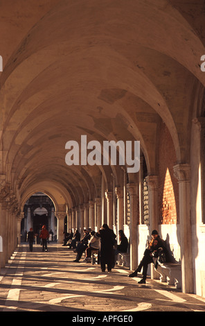 VENEDIG, ITALIEN. Menschen genießen die Wintersonne in eine Kolonnade von Palazzo Ducale (Dogenpalast) am Markusplatz entfernt. Stockfoto