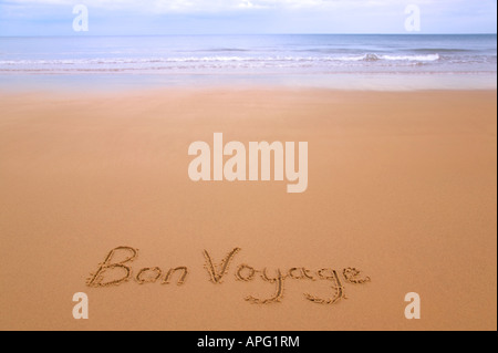 Bon Voyage geschrieben in Sand auf einem goldenen Sandstrand, Meer und Horizont in der Ferne Stockfoto