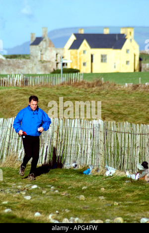 Mann läuft mit Sker Haus in der Ferne Porthcawl Glamorgan Süd wales Großbritannien uk Stockfoto