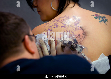 Ein Tätowierer bei der Arbeit, der ein Design auf die Schulter einer Frau färben kann. Bild von Jim Holden. Stockfoto