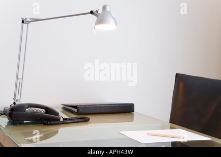 Schreibtisch mit Lampe und schwarzem Leder Drehstuhl. Weiße Wand im Hintergrund. Stockfoto