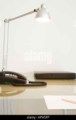Beschnitten, Schreibtisch mit Telefon, pad Lampe und Hinweis gegen weiße Wand. Stockfoto