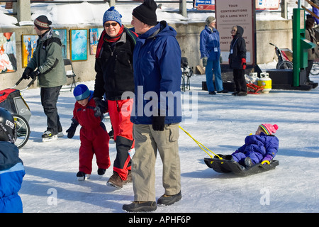 Familie mit zwei Kindern, die ein Kind lernt Skaten ist das andere auf einem Schlitten gezogen Stockfoto