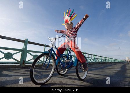 Ein kleiner Junge in einem Indianer Kopfschmuck schreien, wie er auf einem Trike auf den Fahrradweg auf Brighton Seafront spielt Stockfoto