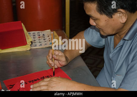 Kalligraph bei der Arbeit, Schreiben von chinesischen Schriftzeichen auf rotem Papier, mit einem traditionellen Kalligraphie-Pinsel. Stockfoto