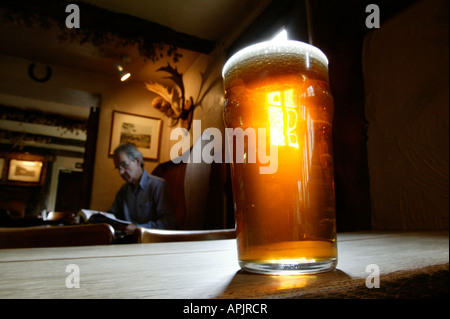 Ein Pint bitter stehend auf einem alten Holztisch in einem englischen Pub. Ein Mann sitzt an einem Tisch hinter. Stockfoto