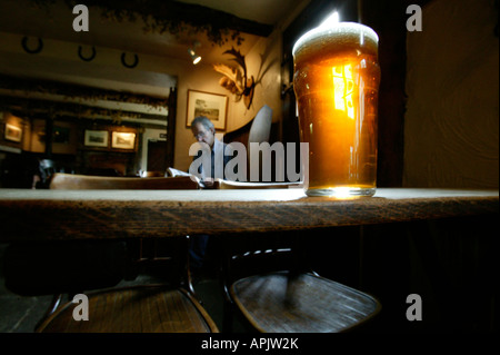 Ein Pint bitter stehend auf einem alten Holztisch in einem englischen Pub. Ein Mann sitzt an einem Tisch hinter. Stockfoto