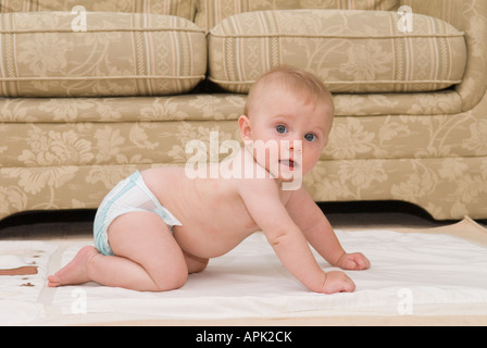 Glückliches Baby in einer Windel auf dem Boden, das kriechen lernt, fünf Monate alt Stockfoto