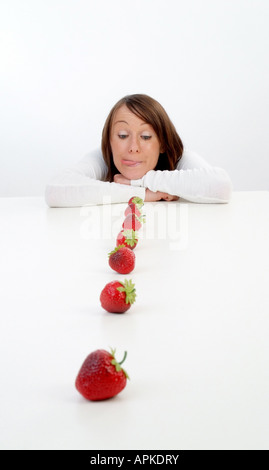 junge Frau sitzt hinter einer Reihe von Erdbeeren Stockfoto