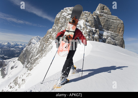 Mann mit Snowboard auf dem Rücken am Schneeschuhwandern in den Bergen, Österreich Stockfoto