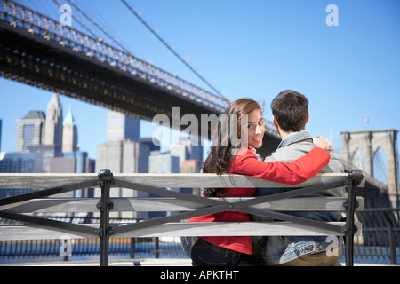 Junges Paar in der Nähe von Brooklyn Bridge, Frau schaut über die Schulter (Rückansicht), New York City, New York, USA sitzen Stockfoto