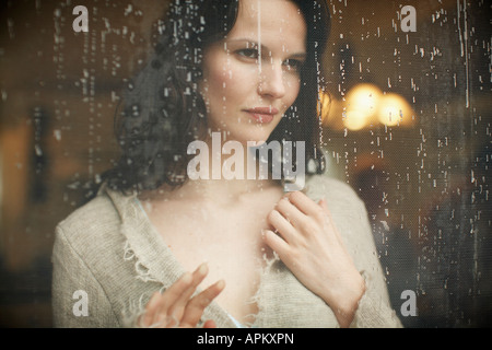 Junge Frau auf der Suche durch das Fenster bei Regen läuft Stockfoto