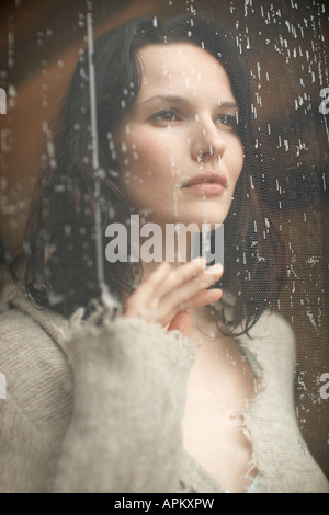 Junge Frau auf der Suche durch das Fenster bei Regen läuft Stockfoto