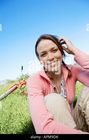 Junge Frau sitzt auf der Wiese, im Hintergrund (Hochformat) Stockfoto