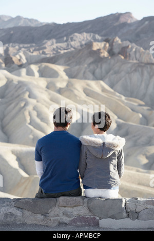 Paar sitzen auf der Mauer aus Stein in der Wüste (Rückansicht) Stockfoto