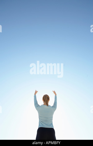 Junge Frau mit erhobenen Armen gegen den klaren Himmel (Rückansicht, Low Angle View) Stockfoto