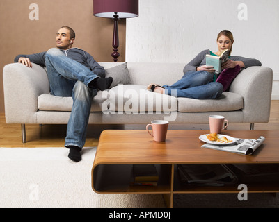 Junge Frau mit Buch und junger Mann beim Anhören von MP3-Player auf dem Sofa Stockfoto