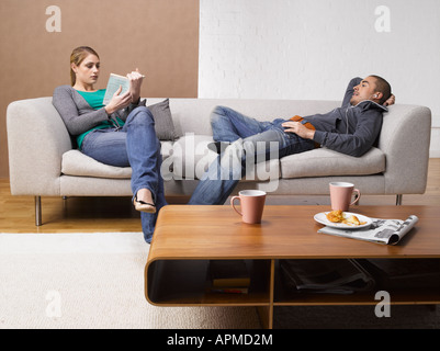 Junge Frau mit Buch und junger Mann beim Anhören von MP3-Player auf dem Sofa Stockfoto