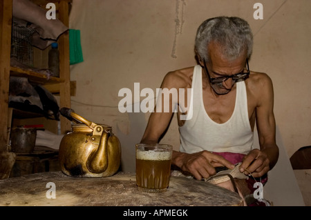 Alter Lederbearbeiter macht Babouches aus Haut der Ziege. Glas Tee Minze und Wasserkocher auf dem Tisch. Fes el Bali Marokko Stockfoto