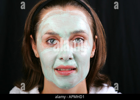 Attraktive junge Frau trägt weißen Bademantel Robe mit leuchtend grünen Avocado Gesichtspackung, lächelte verwöhnen Stockfoto