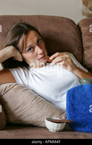 Junge Frau mit schmerzhaften monatliche Regelblutung Regelschmerzen Magenkrämpfe isst Schokolade und lindert Schmerzen mit einer Wärmflasche Stockfoto