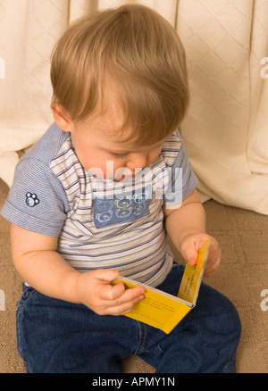 Der elfmonatige Junge hält ein kleines Buch und sieht es sich an Stockfoto