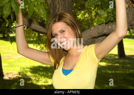 Niedliche Mädchen lächelnd in den Park mit ihren Armen in einem Baum Stockfoto