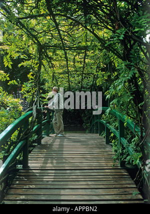 Ein Mann, der unter dem Vordach des Baumes und auf der japanischen Holzbrücke, die Kreuze den Seerosenteich in Claude Monet s Wassergarten gespeist wird der Fluss Epte in Giverny Stockfoto