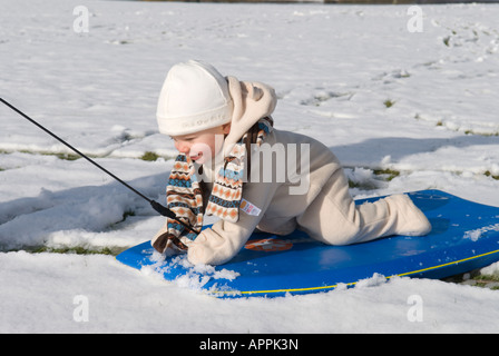 Ein einjähriger Junge, der zum ersten Mal auf einem Schlitten gezogen wird und auf Schnee herabblickt Stockfoto