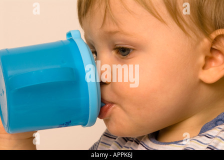 Der elfmonatige Junge hält seinen eigenen Trinkbecher mit Trinkschnabel Stockfoto