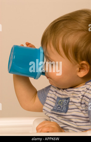 Der elfmonatige Junge hält seinen eigenen Trinkbecher mit Trinkschnabel Stockfoto