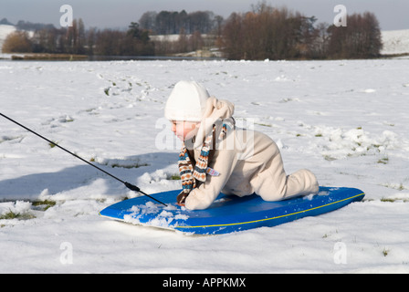 Todler, Baby, auf Schlitten über Schnee gezogen, warm gekleidet mit Hut und Handschuhen, Stockfoto
