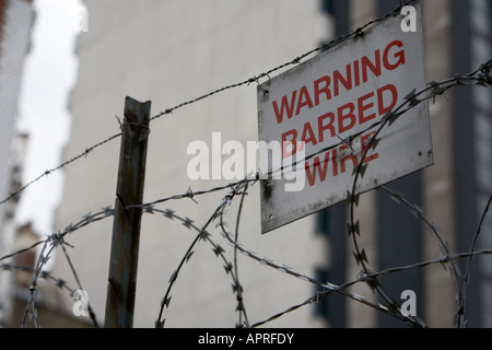 Warnung Stacheldraht Schild zu Stacheldraht befestigt und Stacheldraht auf einem Zaun umliegenden Gebäuden Belfast Nordirland Vereinigtes Königreich Stockfoto