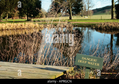 Teich im Spätwinter mit Warnschild 'Danger Tiefwasser' am Rand. West Dean Gardens, Sussex, England, Großbritannien Stockfoto