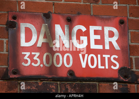 alten verwitterten verrosteten Gefahr, dass 33000 Volt Warnzeichen angebracht, ein roten Backstein Belfast Nordirland UK Wand Stockfoto