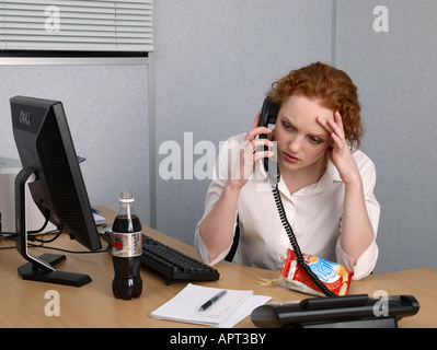 Junge Frau am Telefon an ihrem Schreibtisch Flasche Cola und Tasche von lo Fett Chips Stockfoto