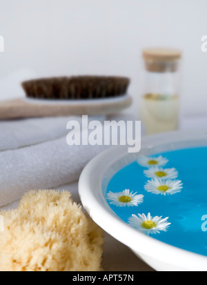 Schüssel mit Wasser mit schwimmenden Blumen, Körperbürste, Naturschwamm und weiße Handtücher Stockfoto