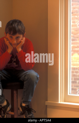 Verschmitztes Lächeln auf kleinen Jungen sitzen auf Stuhl in der Ecke Stockfoto