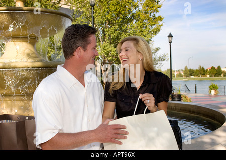 glückliches junges Paar sitzt am Brunnen im Freieneinstellung mit Einkaufstüten Stockfoto