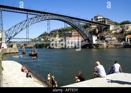Touristen und einheimische Sonnenbaden am Douro-Fluss-Ufer in der Nähe von D. Luiz ich Brücke in Porto, Portugal. UNESCO-Welterbe. Stockfoto
