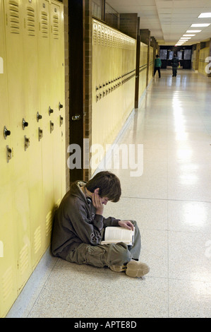 Männliche Schüler setzt sich auf Boden in seinem Spind in der Halle Weg und Studien während seiner Mittagspause Stockfoto