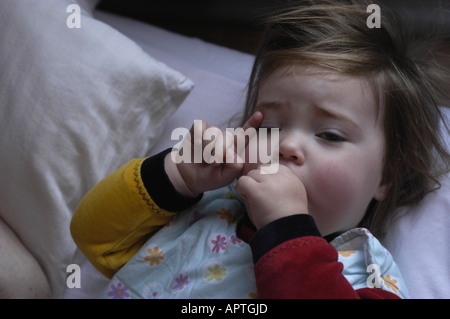 Zwei Jahre alten kaukasischen weibliches Baby saugen ihre Daumen und rieb ihr Auge gleich nach dem Aufwachen am Morgen. Stockfoto