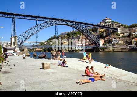 Touristen und einheimische Sonnenbaden am Douro-Fluss-Ufer in der Nähe von D. Luiz ich Brücke in Porto, Portugal. UNESCO-Welterbe. Stockfoto