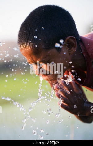 Indischen jungen Gesicht waschen aus einem Tontopf neben einem Reisfeld paddy Stockfoto