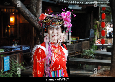 Eine junge Frau in traditioneller Kleidung der Naxi grüßt Menschen mit einem strahlenden Lächeln. Lijiang, Yunnan, China. Stockfoto