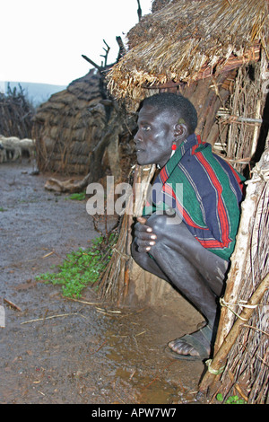 Toposa Mann hocken vor seiner Hütte, Sudan Stockfoto