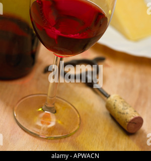 NAHAUFNAHME VON GLAS ROTE ROSEWEIN NEBEN KORKENZIEHER UND WEIN FLASCHE MIT KÄSEPLATTE IM HINTERGRUND Stockfoto
