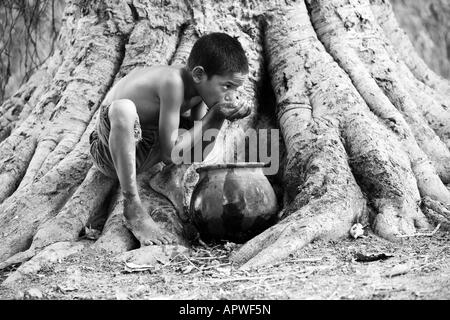 Indianerjunge Trinkwasser aus einem Tontopf auf Banyanbaum. Andhra Pradesh, Indien. Schwarz / weiß Stockfoto